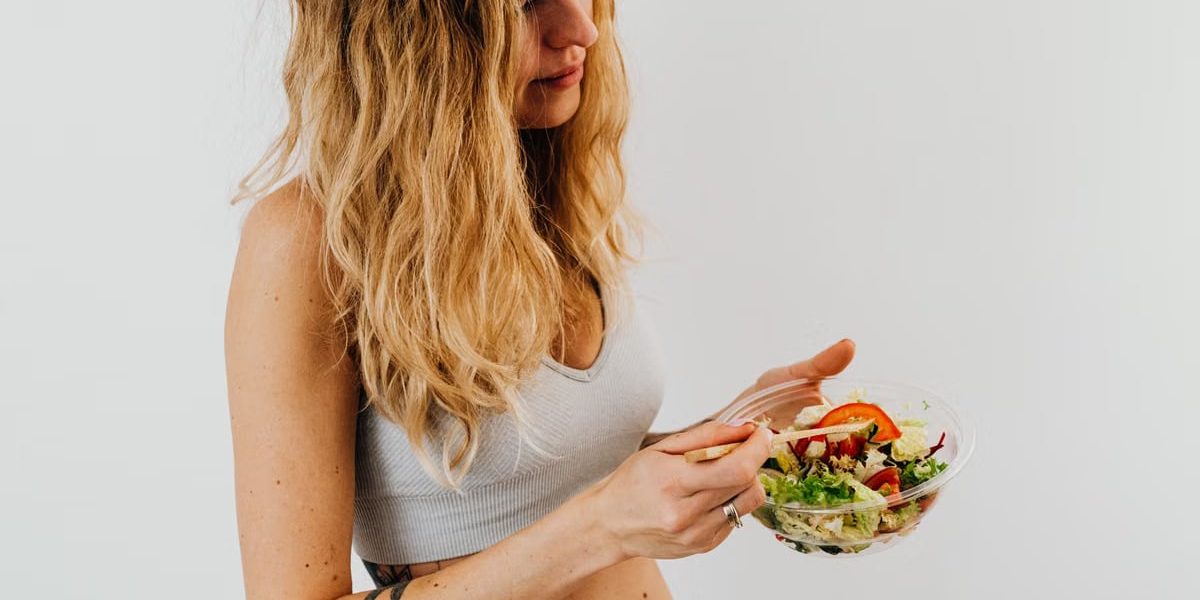 A caucasian woman in a sports bra enjoying a fresh salad, embodying healthy eating and lifestyle.