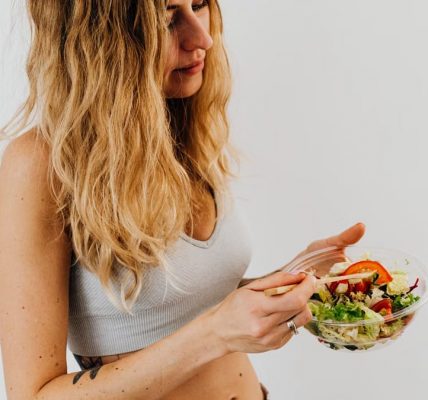 A caucasian woman in a sports bra enjoying a fresh salad, embodying healthy eating and lifestyle.