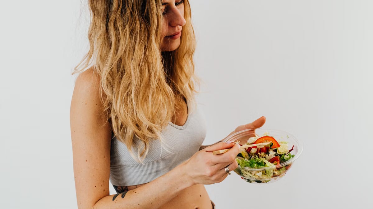 A caucasian woman in a sports bra enjoying a fresh salad, embodying healthy eating and lifestyle.